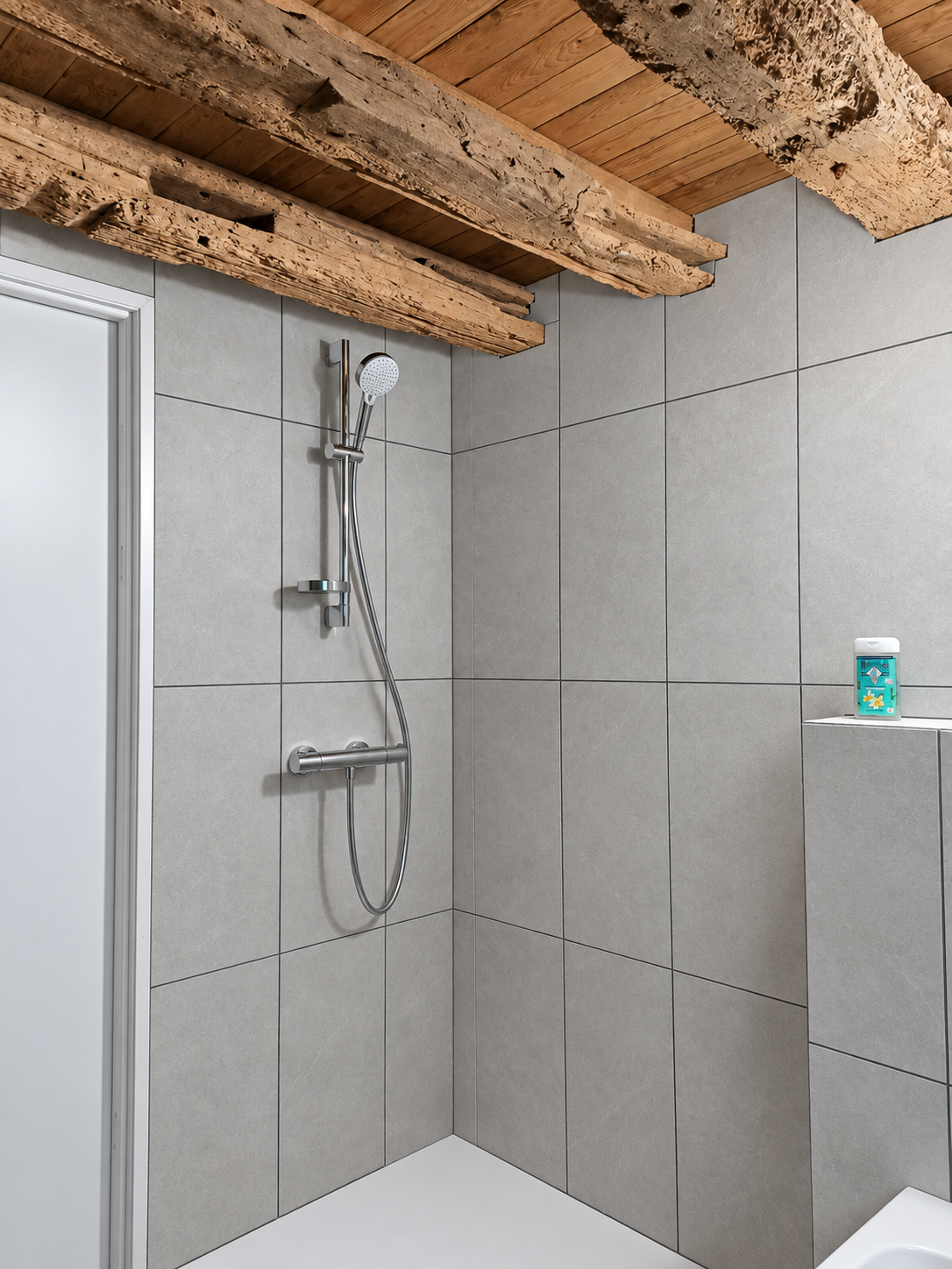 Murs de douche revêtus de faïence gris clair sous des poutres apparentes.