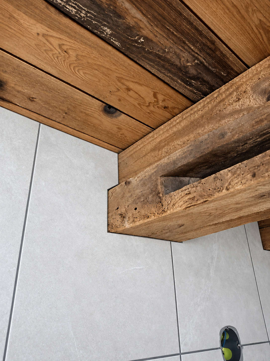 Découpe de faïence gris clair autour d’une poutre, sous un plafond en planches.