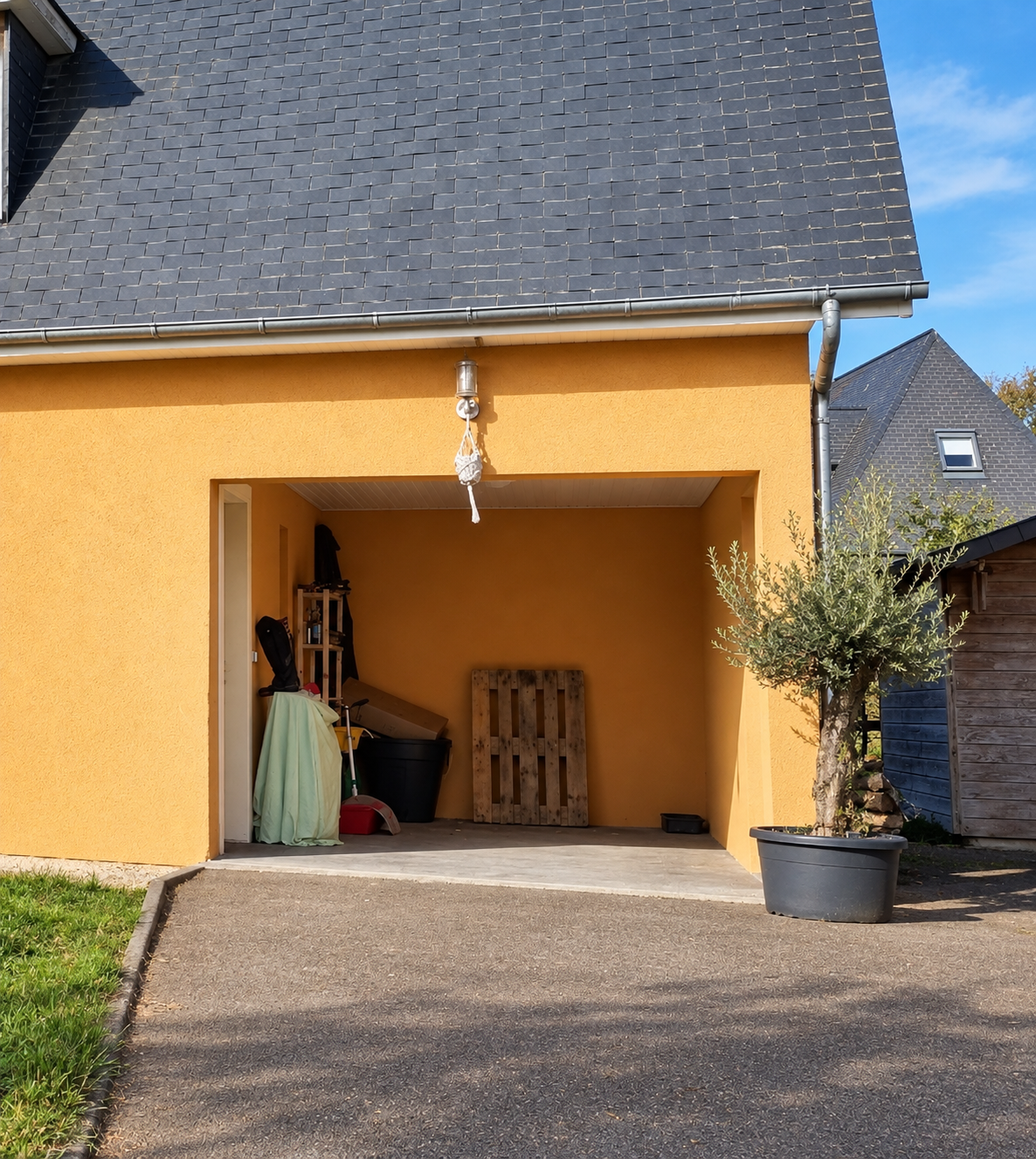 Patio couvert ouvert sur l’extérieur, avec des objets entreposés sous la toiture.