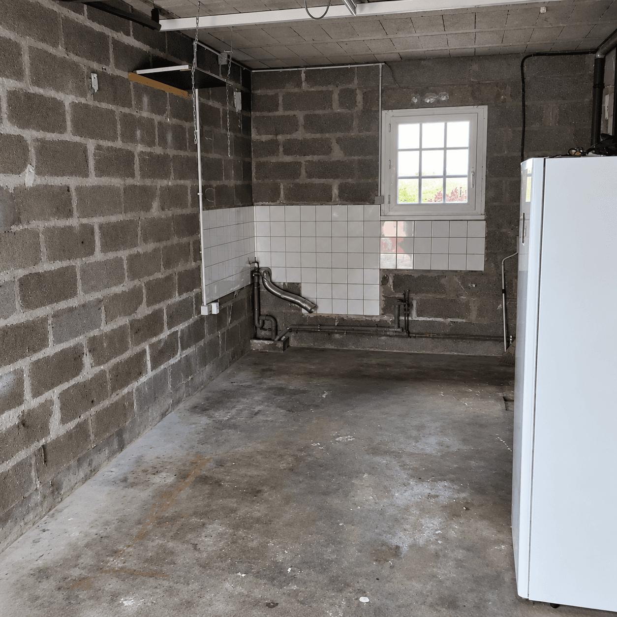 Garage brut avec dalle béton, murs en parpaings et réseaux apparents avant les travaux