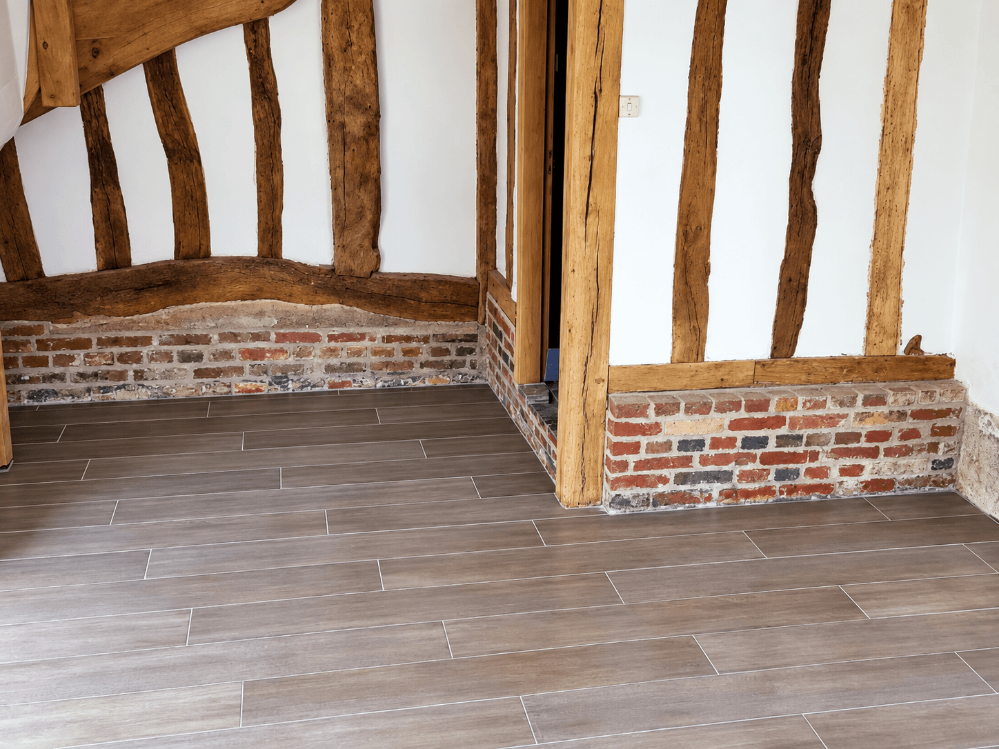 Carrelage imitation parquet intégré aux colombages et aux briques anciennes de la longère